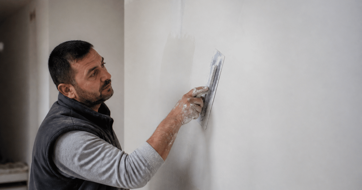 Ouvrier appliquant enduit blanc lisse sur surface murale avec spatule