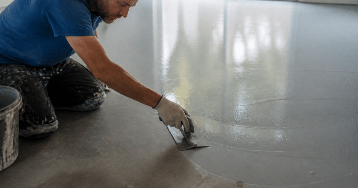Artisan appliquant resine grise lisse sur sol beton avec spatule