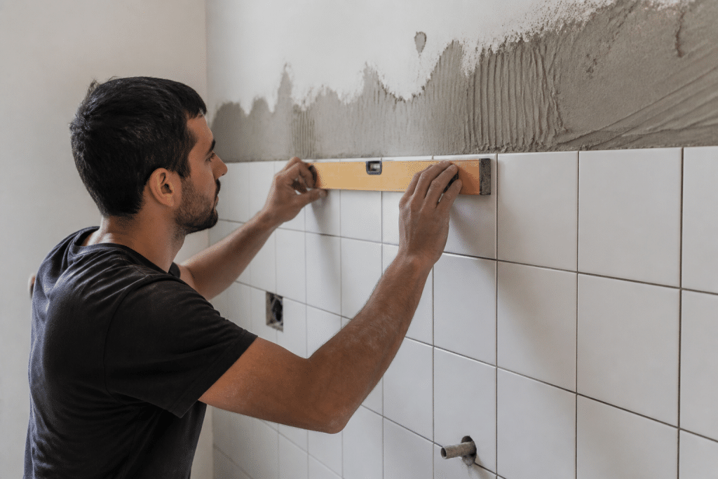 Ouvrier alignant carreaux blancs sur mur avec niveau
