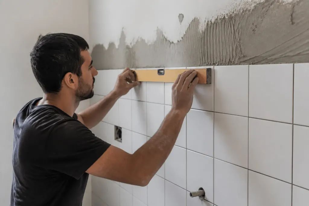 Ouvrier alignant carreaux blancs sur mur avec niveau