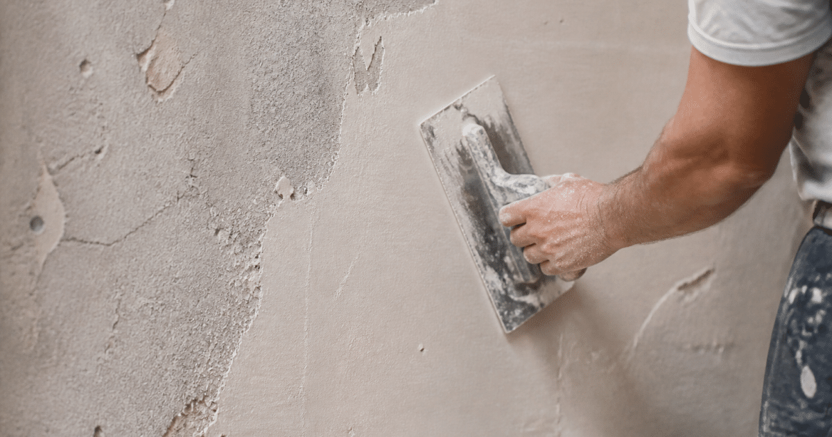 main appliquant enduit clair sur surface murale rugueuse