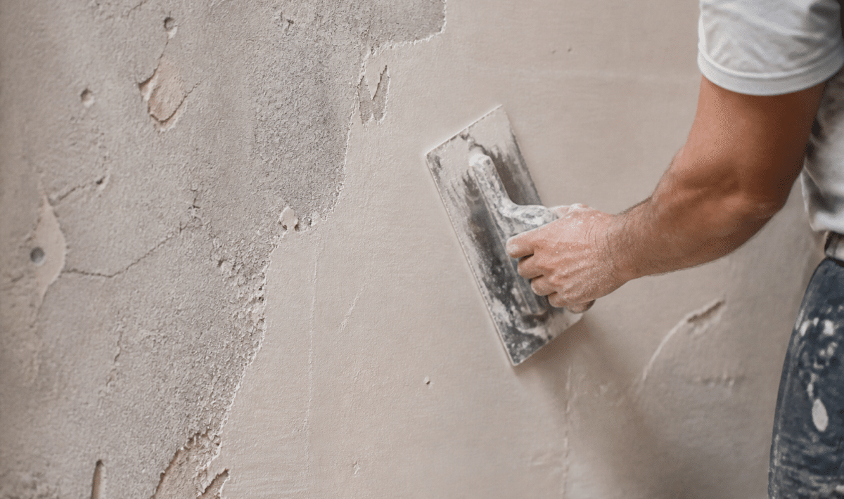 main appliquant enduit clair sur surface murale rugueuse