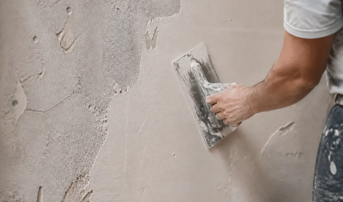 main appliquant enduit clair sur surface murale rugueuse