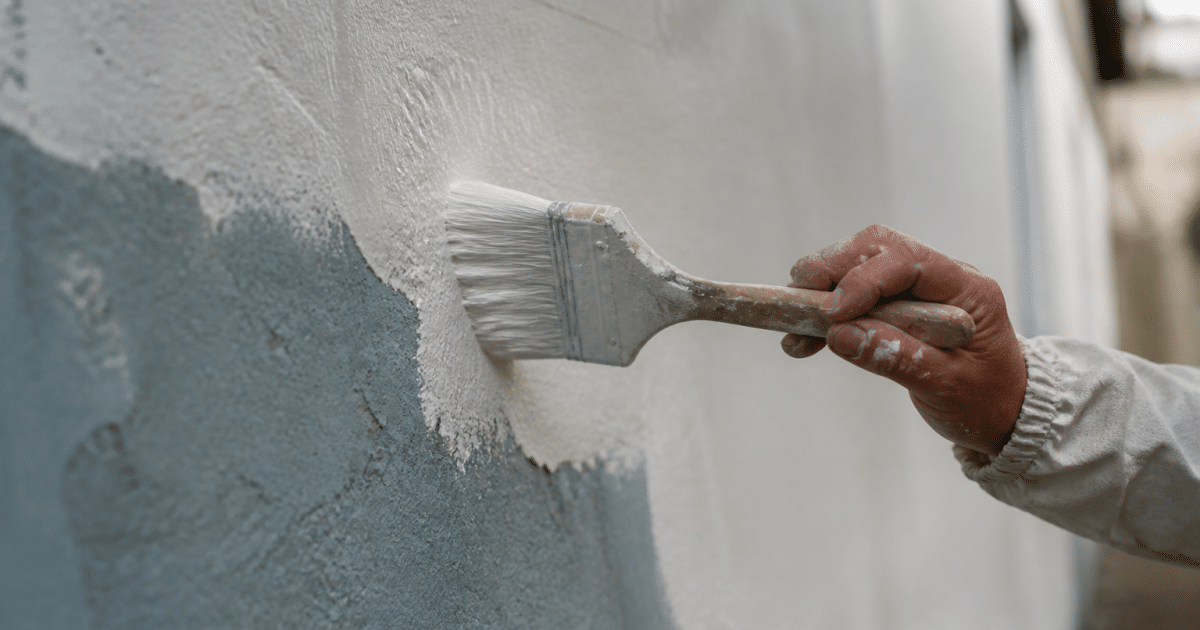 Pinceau appliquant enduit blanc sur mur vertical peint
