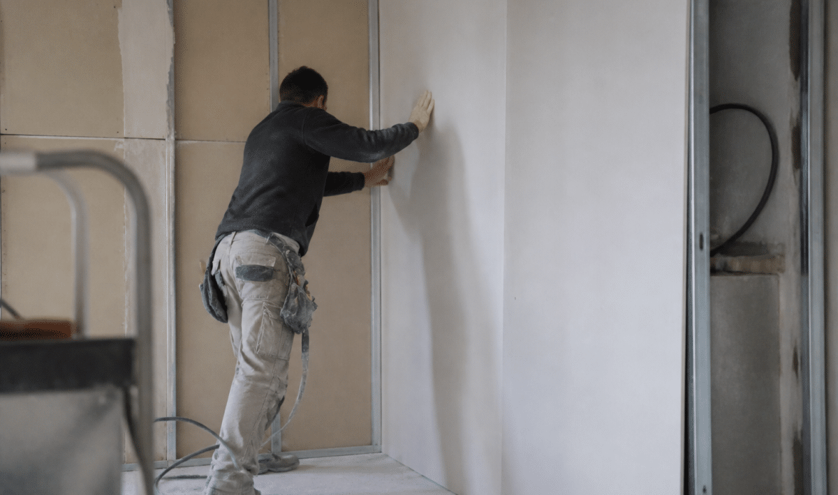 ouvrier installe plaques placo verticales sur structure murale intérieure