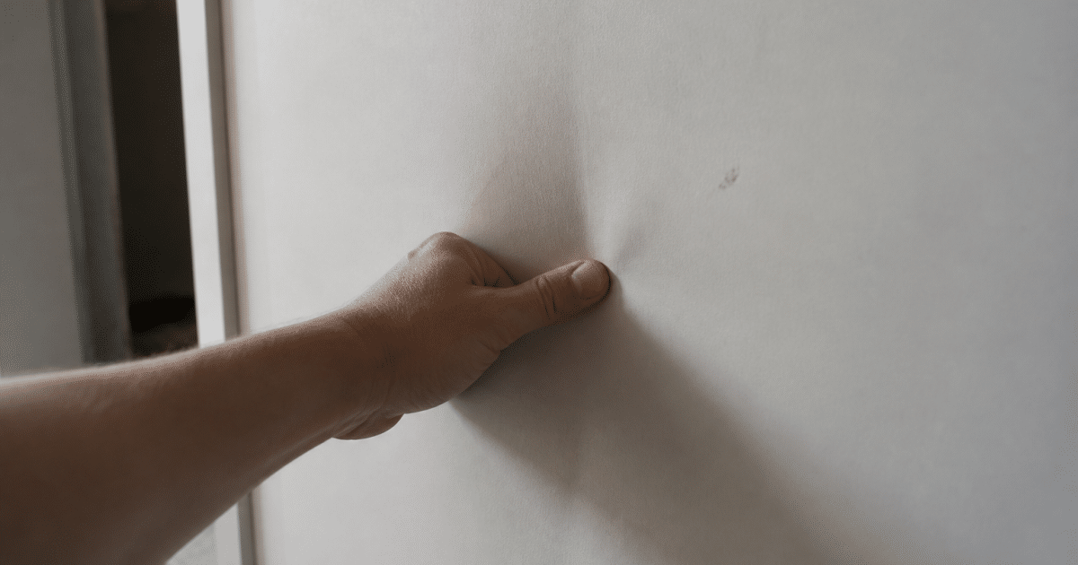 Main appuyant sur plaque de platre qui se deforme vers l'interieur