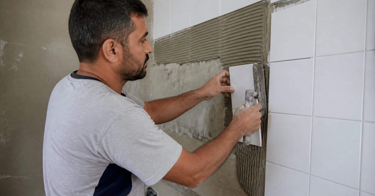 Ouvrier appliquant carreaux blancs sur mur vertical avec spatule
