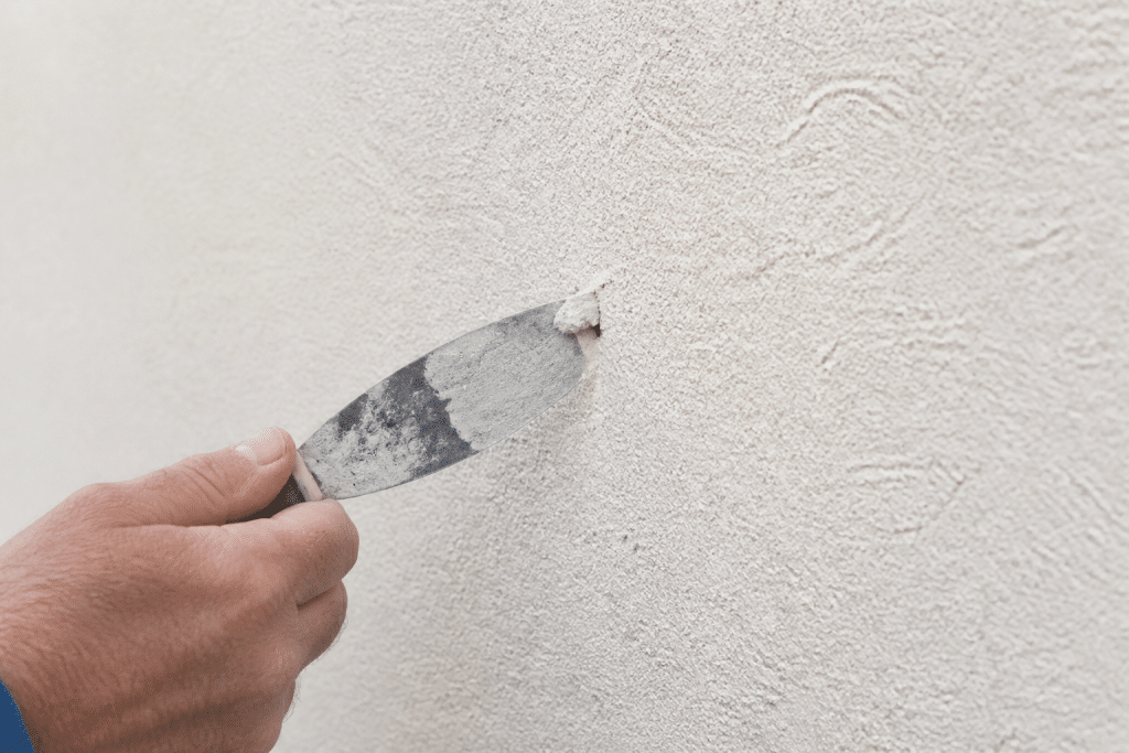 Spatule remplissant petit trou crepi mur blanc