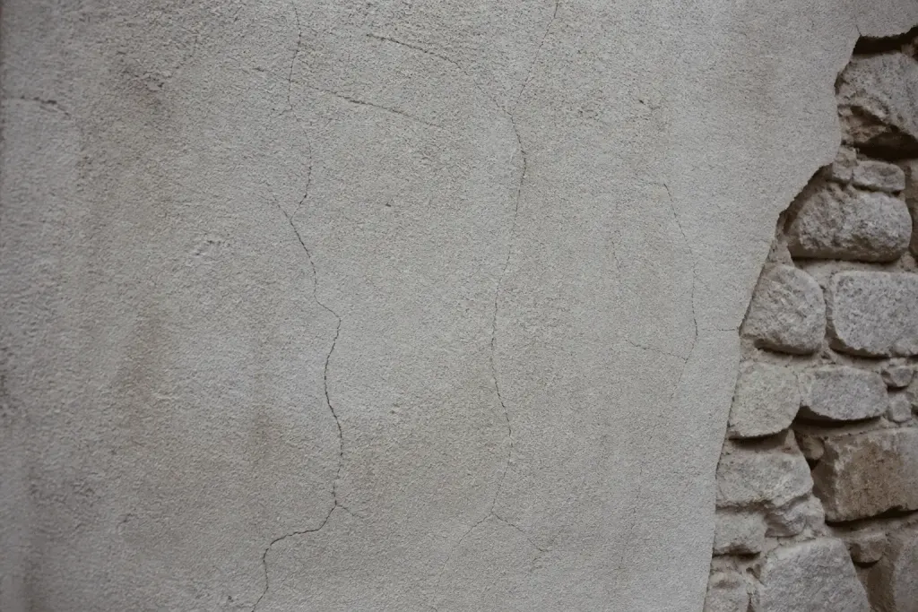 Mur avec fissures de retrait dans couche épaisse d'enduit